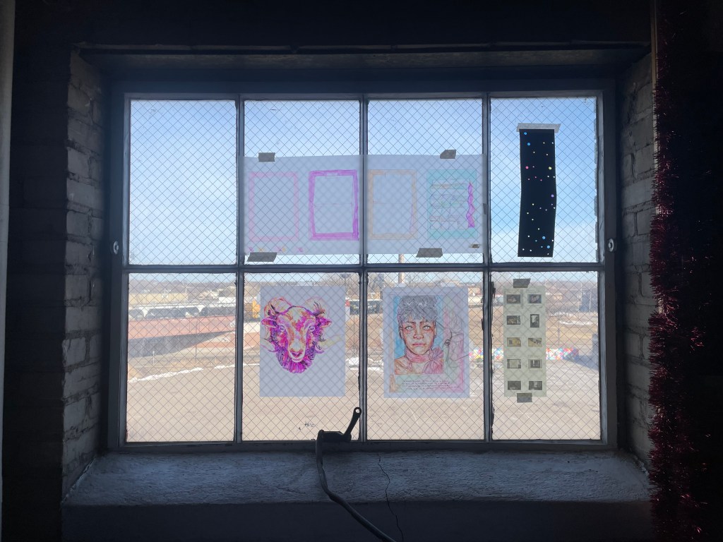 Zoomed out image of Squeaky Wheel hanging on a window in Grover’s Studio